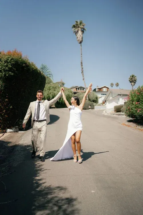 Couple holding hands and cheering on a sunny suburban street, with a tall palm tree in the background