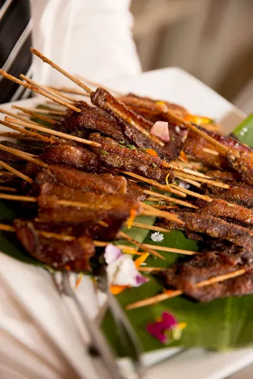 Skewered grilled meat on a white plate, garnished with green leaves and flowers