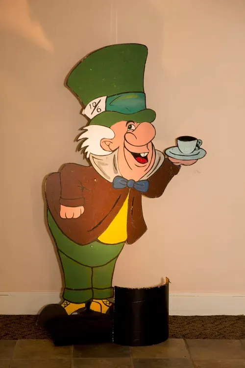 Cartoon old man cutout with green hat, brown coat, and teacup on a beige wall background