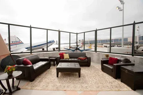 Airport lounge with dark sofas, coffee table, and large windows overlooking planes on the tarmac
