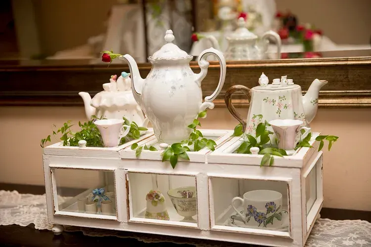 White tea set on a white tray with green ivy accents, displayed on a lace-covered table.