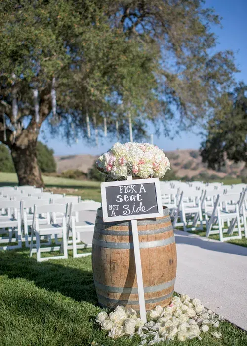 Wedding sign on wooden barrel with white flowers along an outdoor aisle