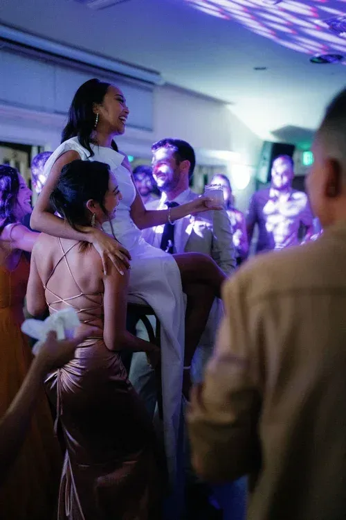 Guests dancing at a party with purple lighting and a woman in a white dress on stage