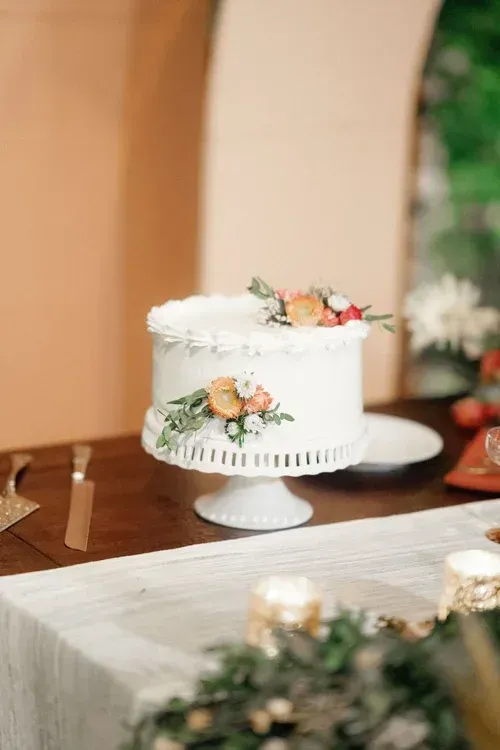 White floral tiered cake on a pedestal at a decorated event table