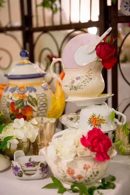 Decorative teacups, teapots, and white flowers with pink roses on a table