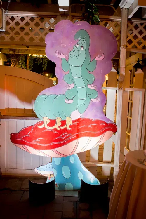 Cartoon cutout of a green caterpillar on a red mushroom with a pink tree backdrop outdoors at night