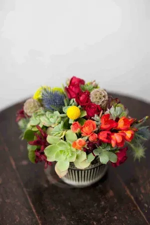 Colorful flower bouquet in a striped vase on a dark wooden table