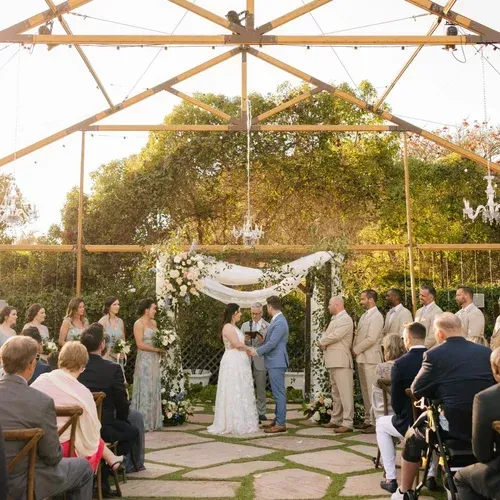 Outdoor wedding ceremony under a wooden pavilion, couple at altar surrounded by seated guests and floral arch