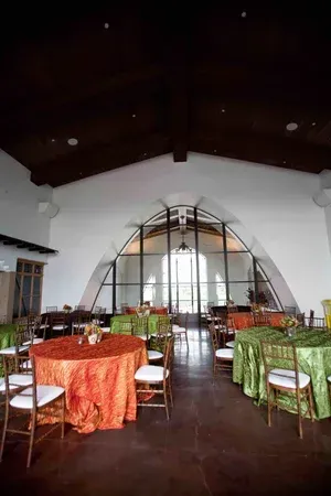 Empty dining hall with round tables, colorful tablecloths, and a tall arched doorway at the back