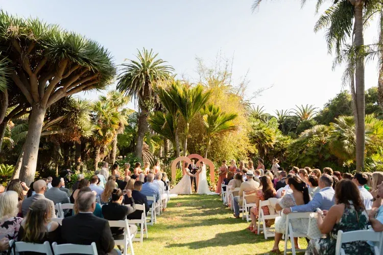 Outdoor wedding ceremony with guests seated in a garden aisle, couple standing under a floral arch