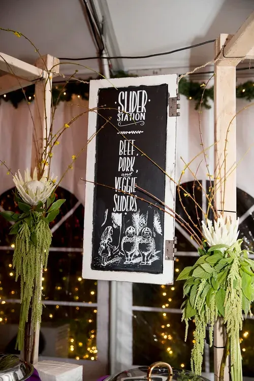 Black event sign on a decorated balcony with fairy lights and hanging greenery