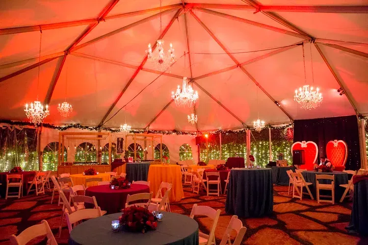 Red-lit tented event space with chandeliers, round tables, chairs, and a dance floor.