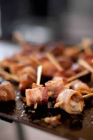 Skewered bacon bites sizzling on a grill, with a blurred background