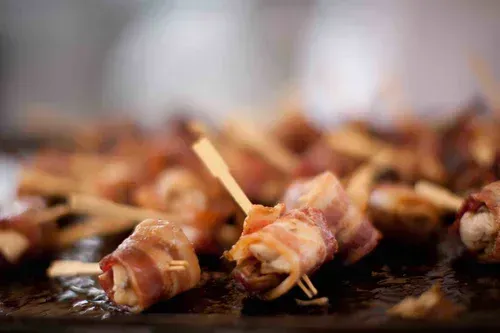 Bacon-wrapped appetizers with toothpicks on a tray, in warm lighting