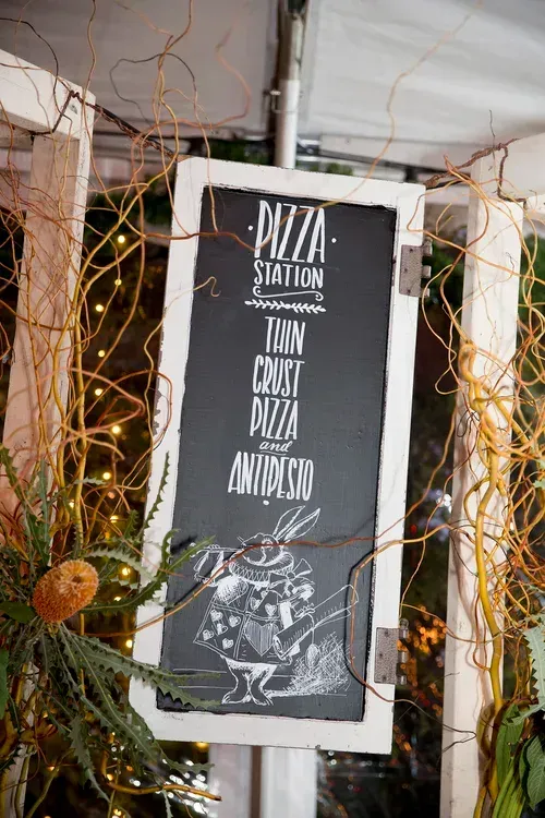 Black-and-white “Pizza Station” sign hanging amid vines and lights.