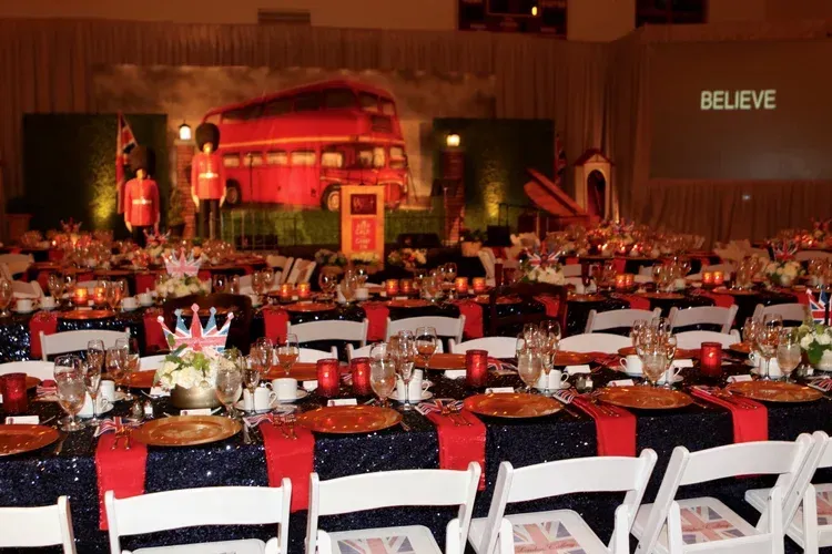 Decorated banquet hall with long tables, red-and-blue chairs, and a stage with a red bus backdrop