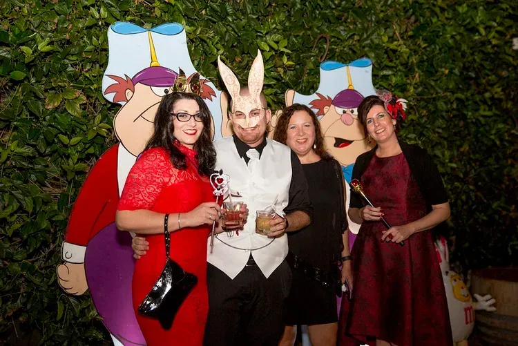 Four women posing in formal dresses with a large white rabbit figure at an outdoor event.