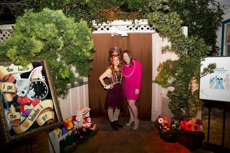 Two women posing in front of a pink backdrop surrounded by colorful floral decorations