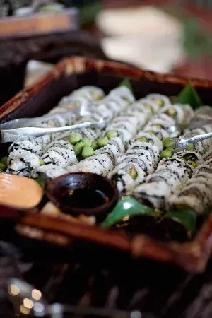 Tray of sushi rolls with white rice and seaweed, garnished with herbs, served with dipping sauces.