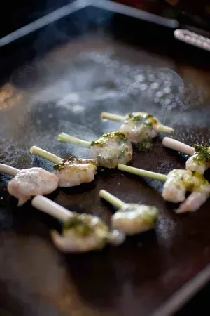 Skewered meatballs on a dark skillet, with a glossy sauce and scattered seasoning