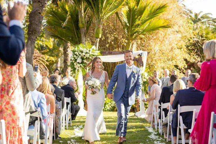 Bride and groom walking down an outdoor aisle at a sunlit wedding ceremony