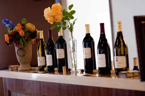 Wine bottles lined on a shelf beside colorful flowers in a warmly lit room
