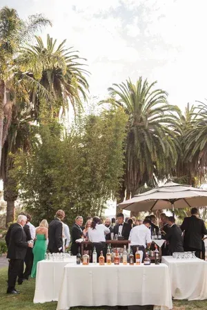 Guests mingling at an outdoor reception with a long white table and palm trees in the background