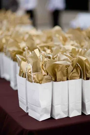 Rows of white gift bags with gold tissue paper on a burgundy tablecloth