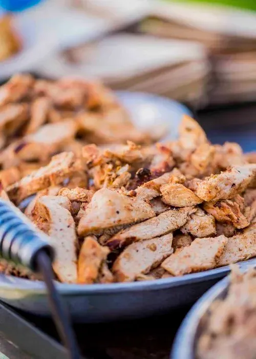 Bowl of sliced seasoned chicken at a buffet, with serving spoon and other dishes blurred in background