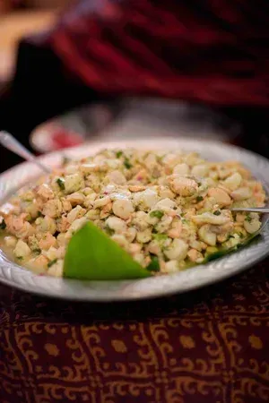 Plate of creamy salad with herbs and a lime wedge on a patterned tablecloth