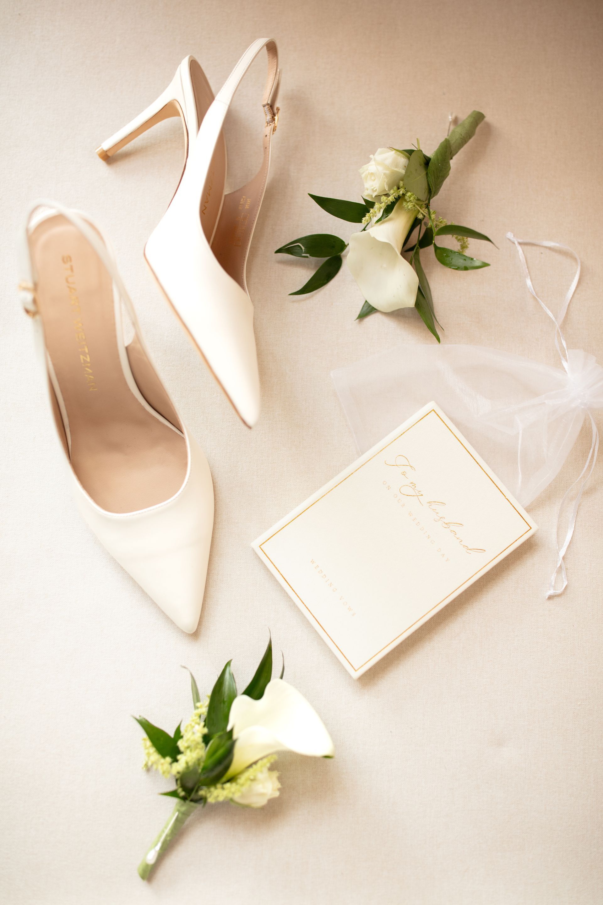 White bridal heels, small floral bouquets, and a white clutch on a soft beige background