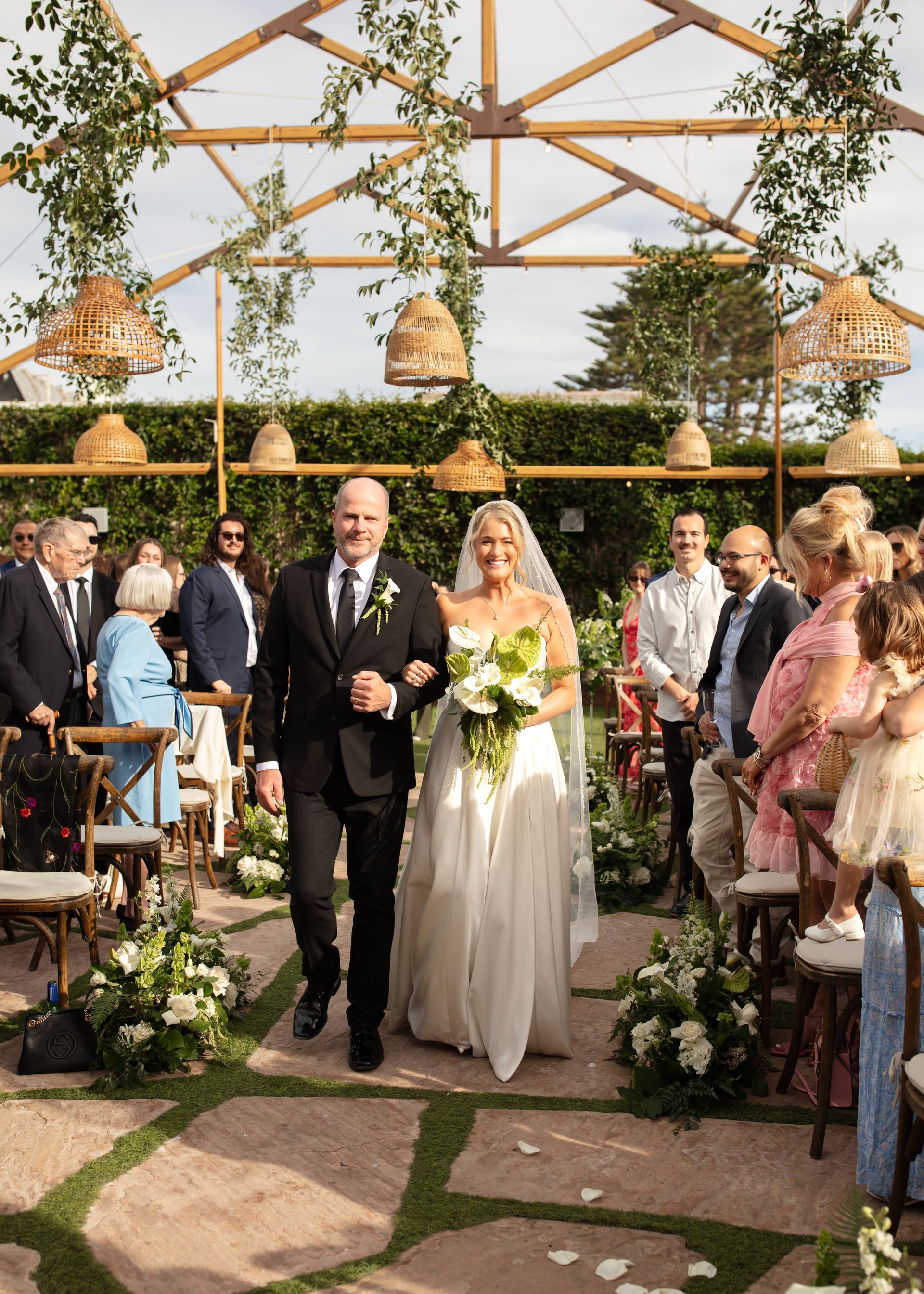 Bride and groom walking down a garden aisle under a wooden arch at an outdoor wedding