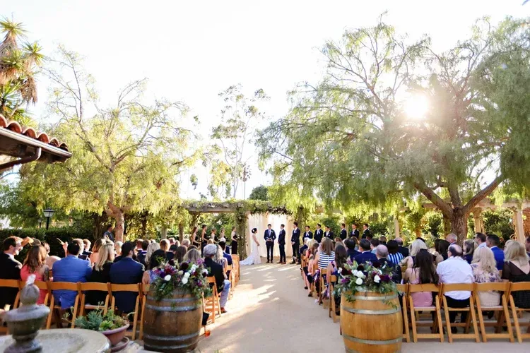 Outdoor wedding ceremony with guests seated on both sides of a sunlit garden aisle
