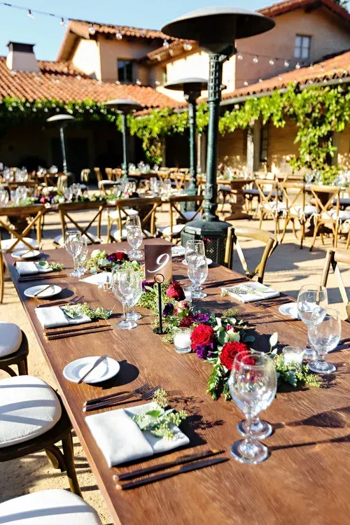 Outdoor restaurant terrace set for a formal meal with neatly arranged tables, wine glasses, and flowers in sunlight