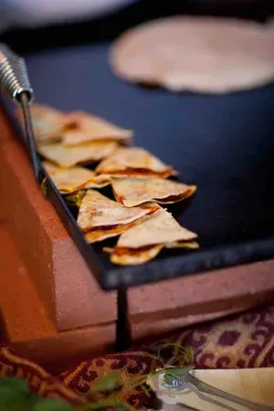 Grilled triangular snacks on a hot skillet with tongs, next to a round flatbread or pancake