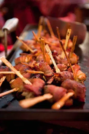 Skewers of grilled meat on a tray at a buffet, with warm orange-brown tones
