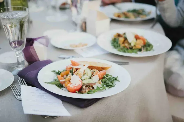 Plated salads on a table set for a meal, with glasses and a purple napkin