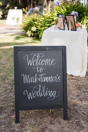 Black welcome sign at an outdoor wedding reads “Welcome to Makenna’s Wedding.”