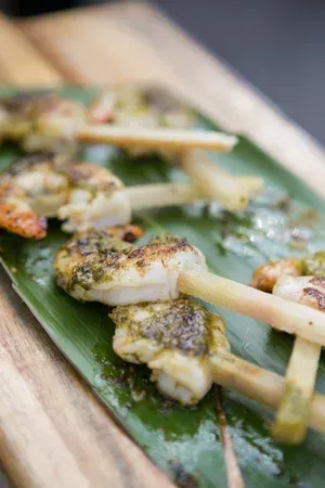 Grilled skewered seafood on a banana leaf, garnished with herbs and seasoning.