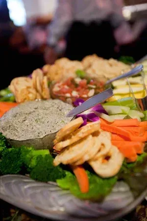 Assorted sliced vegetables, meats, and dips arranged on a platter at a buffet