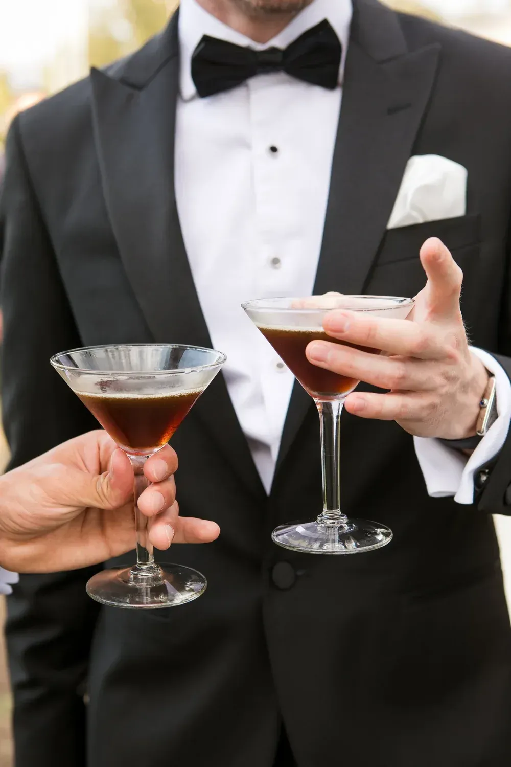 Tuxedoed person holding two martini glasses at a formal event