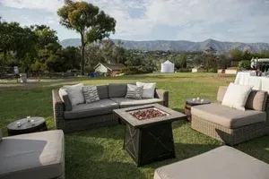 Outdoor patio with gray and beige sofas around a fire table on a lawn with mountain views
