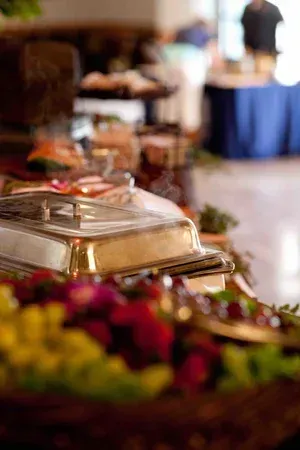 Chafing dish on a buffet table with colorful flowers in the foreground and a blurred dining area behind