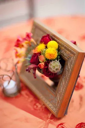 Wooden photo frame with a small bouquet of yellow, red, and white flowers on a peach tablecloth
