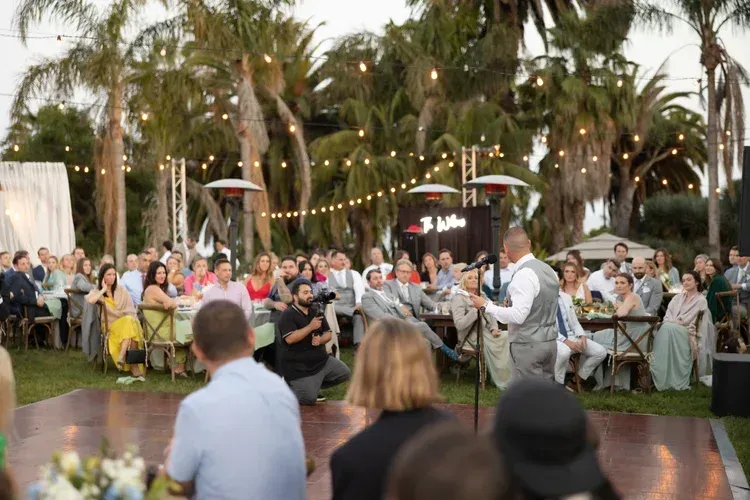 Outdoor wedding ceremony with guests seated around a lit dance floor under palm trees at dusk