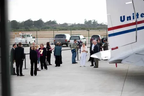 People gathered on an airport tarmac beside a United plane tail and nearby vehicles.