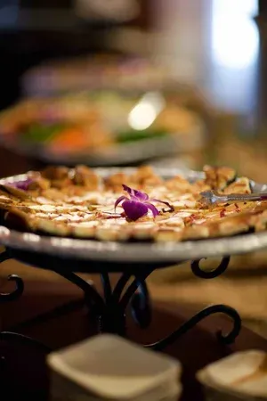 Pizza on a decorative stand with a purple garnish in a warmly lit restaurant setting