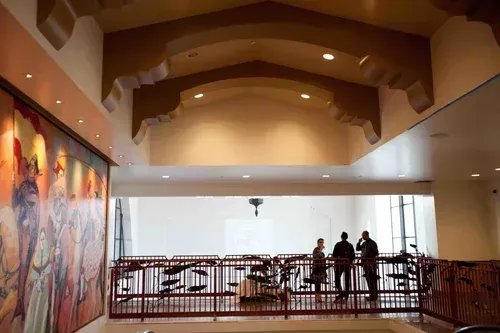 Spacious atrium with curved wooden ceiling, mural wall, and a few people standing by a railing.