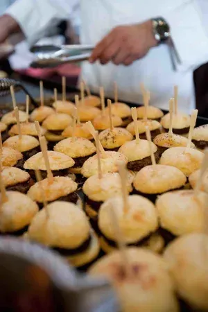 Mini appetizers on skewers arranged on a tray, with a server holding tongs in the background.