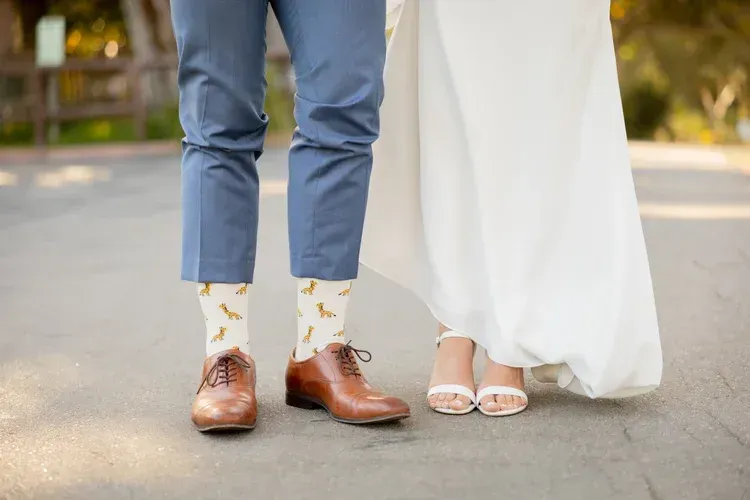 Bride and groom's lower legs and feet, with brown shoes and a white dress on a paved path